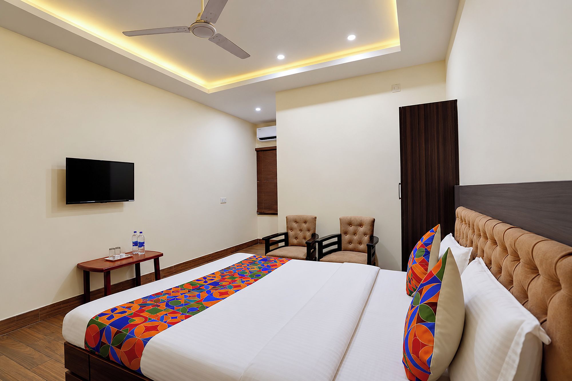 A hotel room with a bed, a television, a ceiling fan, and a seating area with chairs.