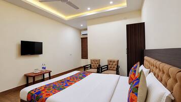 A hotel room with a bed, a television, a ceiling fan, and a seating area with chairs.