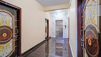 Un pasillo con puertas ornamentadas, una pared de mármol y un ascensor moderno.