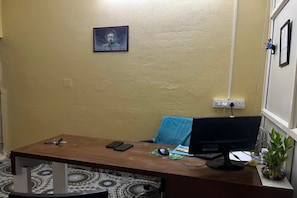 Una habitación con un escritorio de madera, una computadora, una silla, un enchufe en la pared y un cuadro en la pared.
