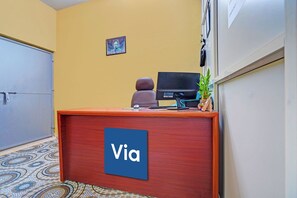 A reception desk with a sign reading 'Via,' a computer monitor, a chair, a small Buddha statue, and a potted plant. - FabHotel Equinox Inn (Bhubaneshwar)