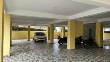 A covered parking area with patterned flooring, yellow pillars, and a white car and motorcycles parked.
