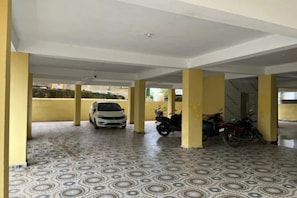 Un área de estacionamiento techada con piso estampado, pilares amarillos y un automóvil blanco y motocicletas estacionadas.