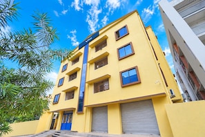 A yellow multi-story building with a blue door and windows, surrounded by greenery. - FabHotel Equinox Inn (Bhubaneshwar)