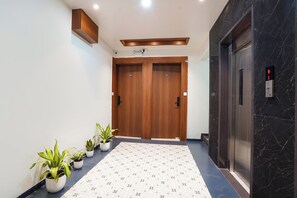 A hallway with a wooden door, an elevator, and potted plants. - FabHotel Infinity Corporate Stay (Pune)