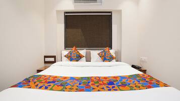 Habitación de hotel con cama, ventana con persiana, mesita de noche con teléfono y un equipo de aire acondicionado en la pared.