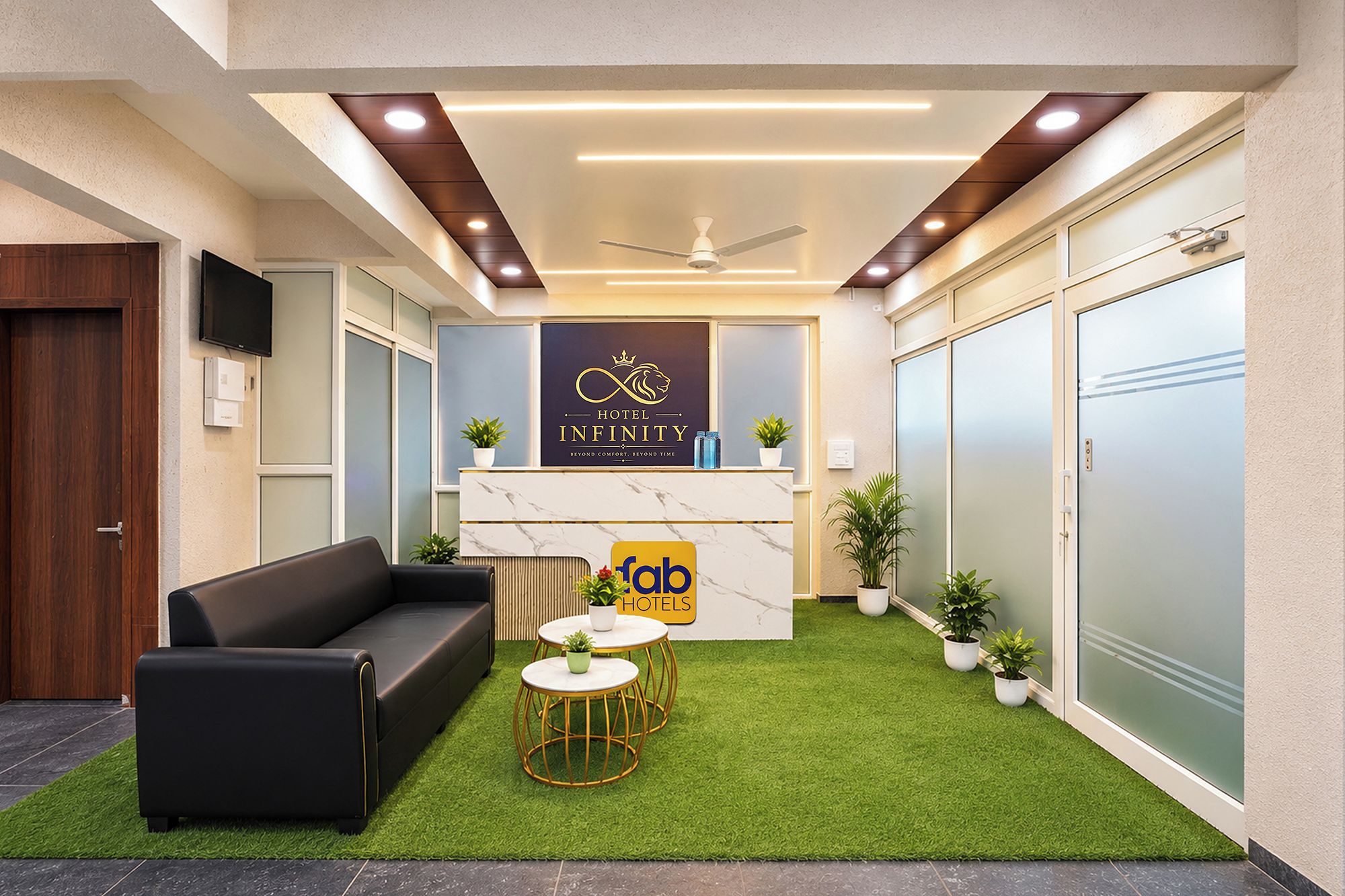 A hotel reception area with a modern design, featuring a reception desk, a black leather sofa, and a small seating area with round tables.