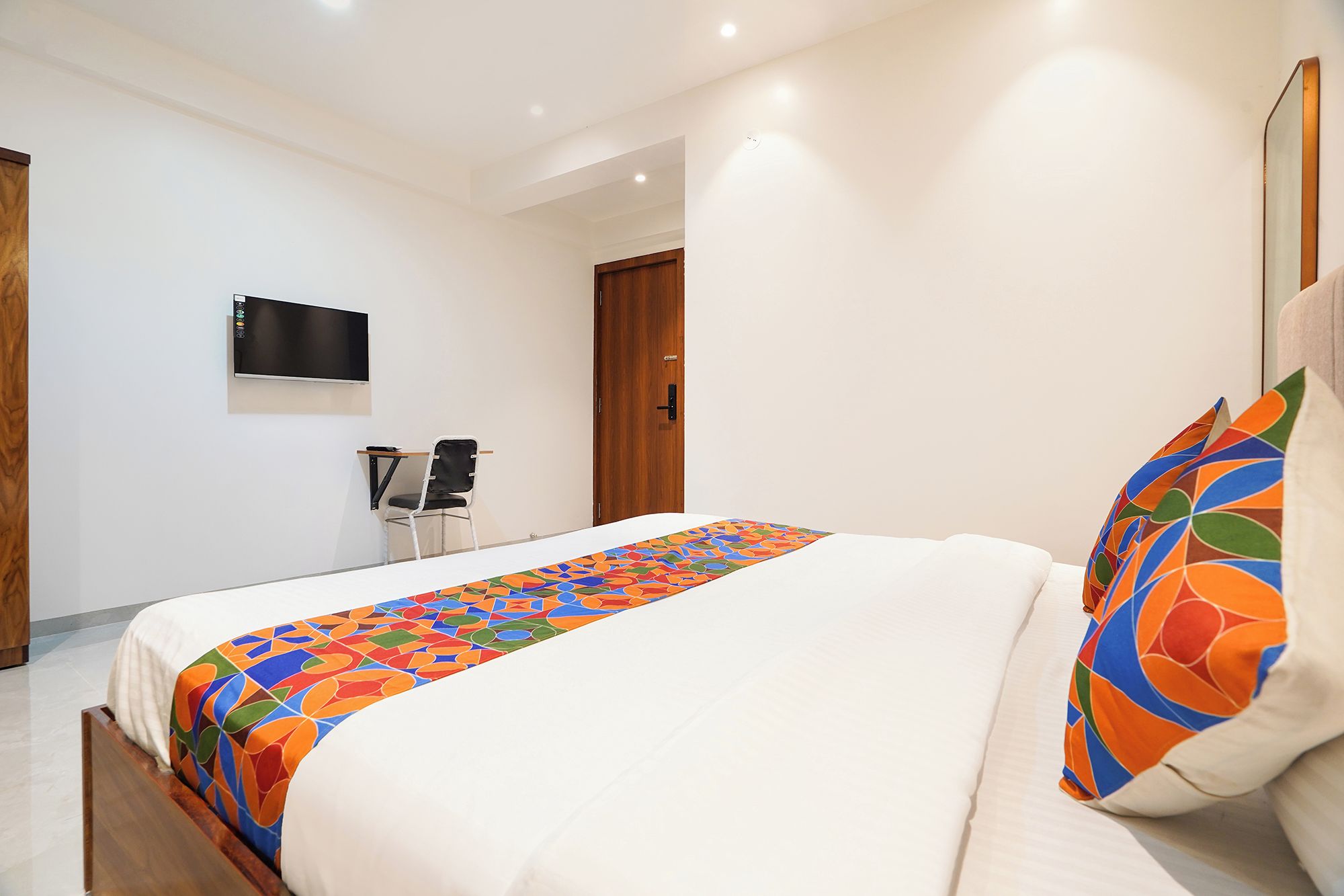 A hotel room with a bed, a desk, a chair, a TV, and a door.