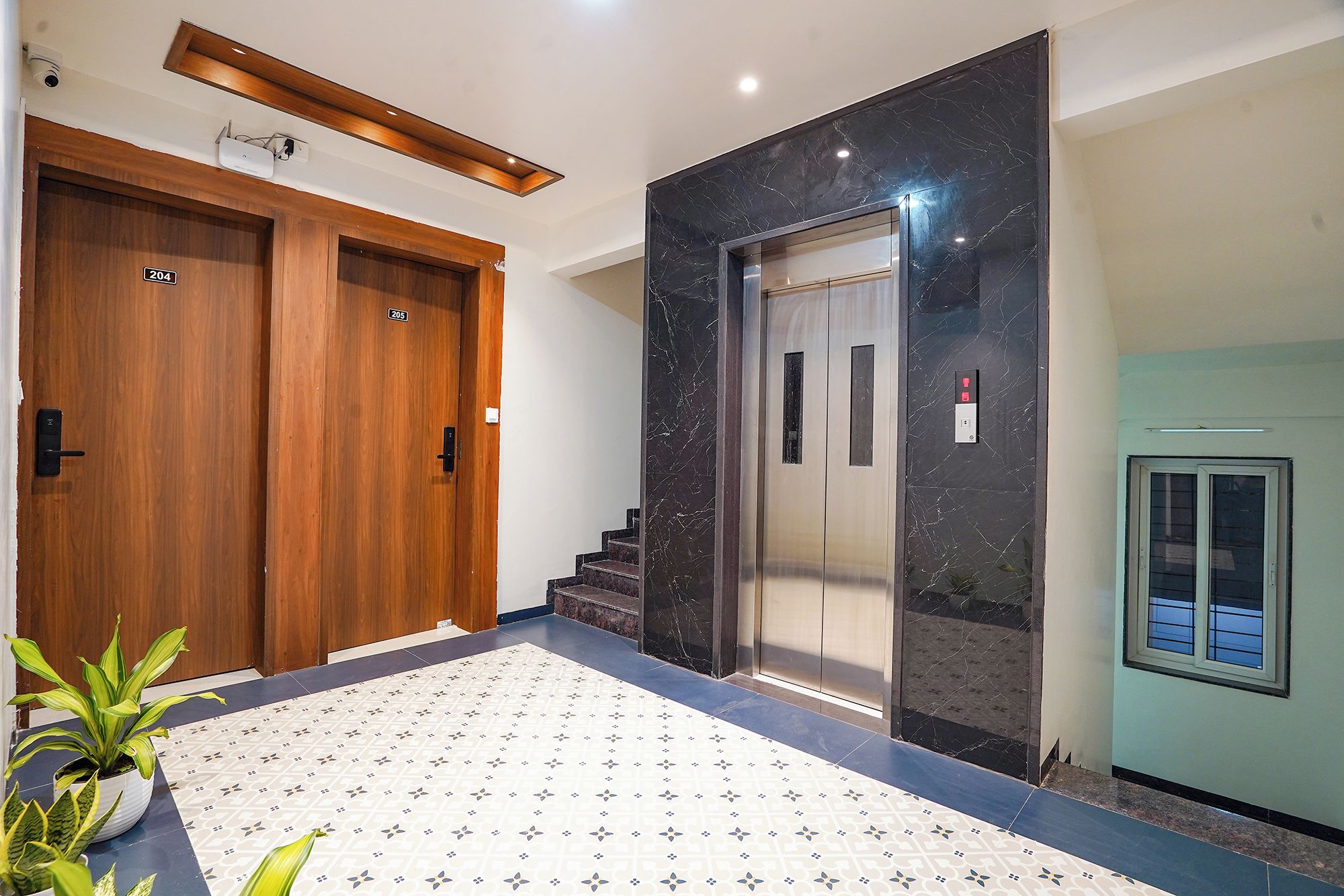 Un vestíbulo de hotel con una puerta de madera con la etiqueta '204', un ascensor de mármol y un suelo de baldosas.