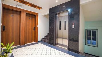 Un vestíbulo de hotel con una puerta de madera con la etiqueta '204', un ascensor de mármol y un suelo de baldosas.