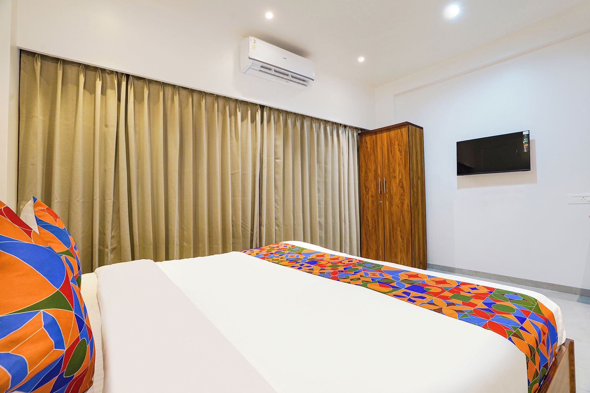 Una habitación de hotel con cama, cortinas, aire acondicionado, televisor y armario.