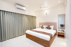 A hotel room with a large bed, a ceiling fan, an air conditioning unit, a bedside table with a coffee maker, and a mirror. - FabHotel Infinity Corporate Stay (Pune)