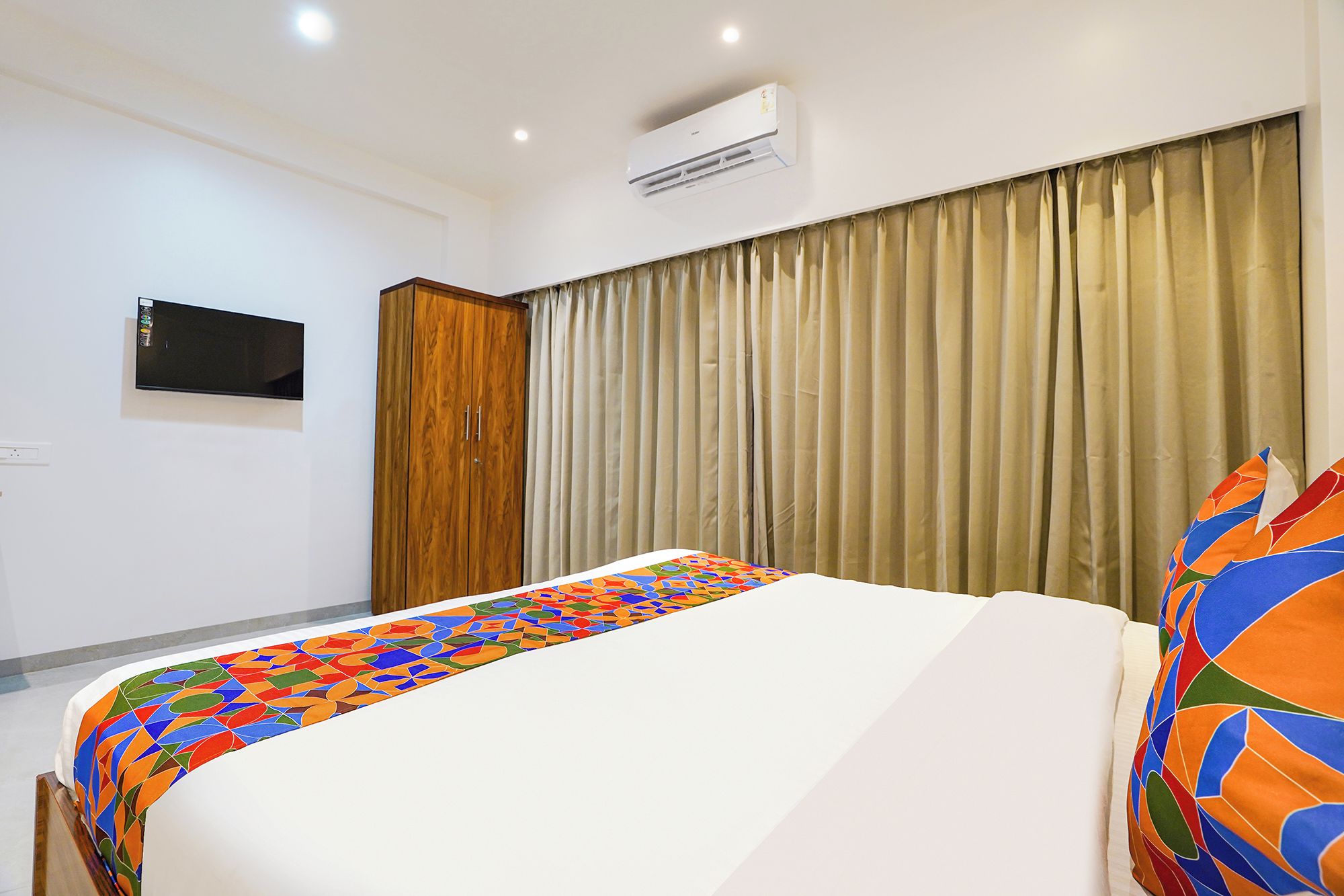 Una habitación de hotel con cama, armario, televisor de pantalla plana y ventana con cortinas.
