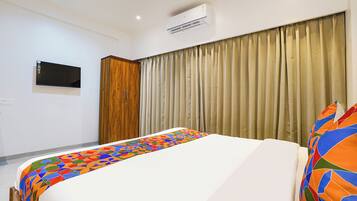 Una habitación de hotel con cama, armario, televisor de pantalla plana y ventana con cortinas.
