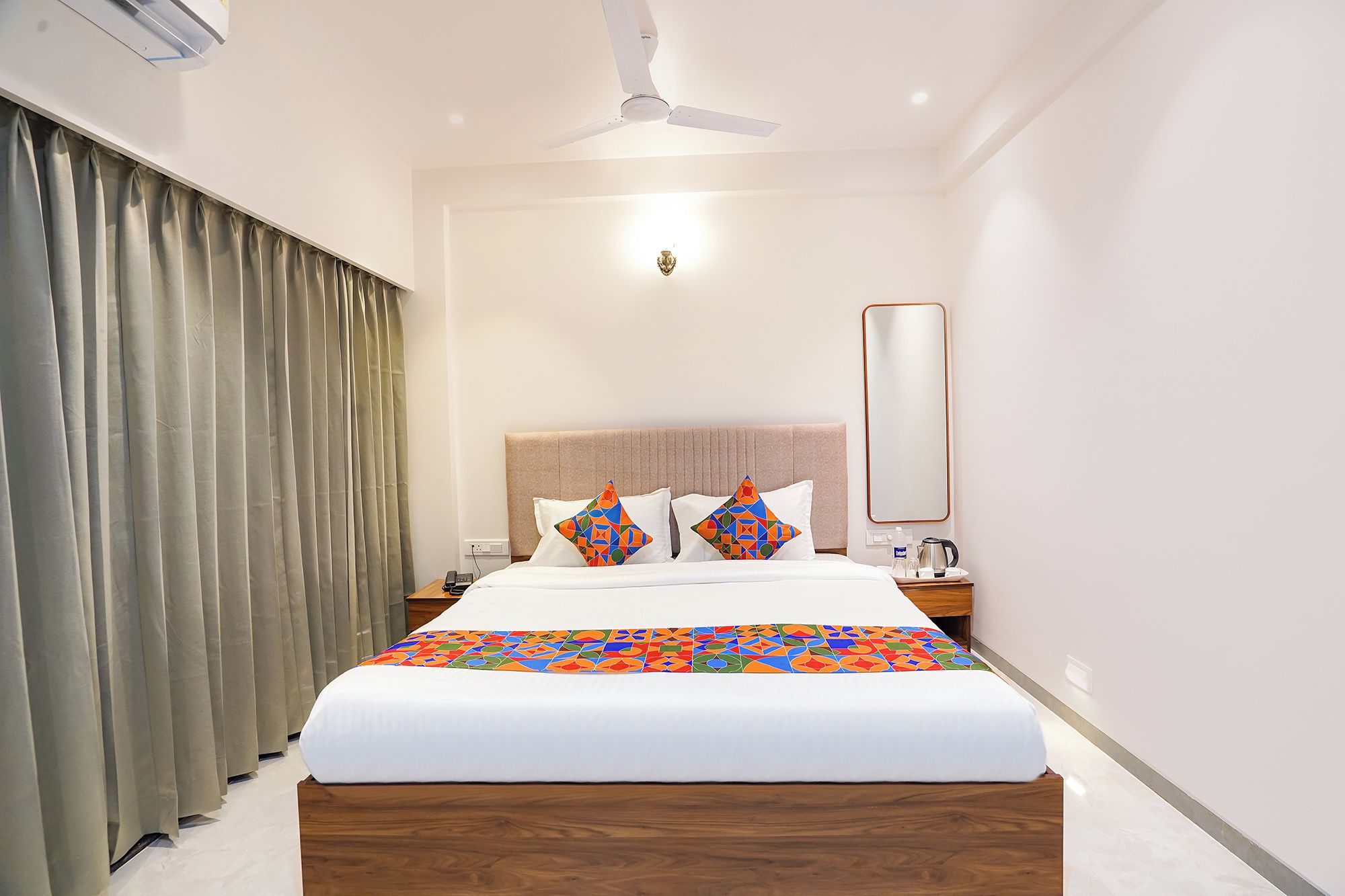 Una habitación de hotel con cama, mesita de noche, espejo y ventilador de techo.