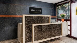 Un mostrador de recepción con un cartel, una planta en maceta y un ventanal con detalles decorativos.