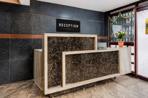A reception desk with a sign, a potted plant, and a patterned wall.