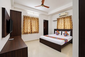 Una habitación de hotel con una cama, televisión, ventilador de techo y cortinas.