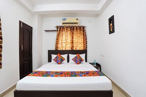 Quarto de hotel com cama, mesa de cabeceira, ar condicionado e janela com cortinas.