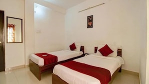 Quarto de hotel com duas camas, cada uma com um cobertor vermelho e lençóis brancos, um quadro pequeno na parede e uma porta com cortina.