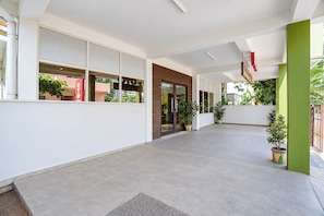 Un amplio pasillo interior con diseño moderno, que incluye una entrada con puerta de vidrio, plantas en macetas y una paleta de colores neutros y luminosos.