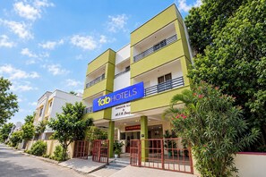 Hotel com placa visível, vários andares e entrada fechada por portão.