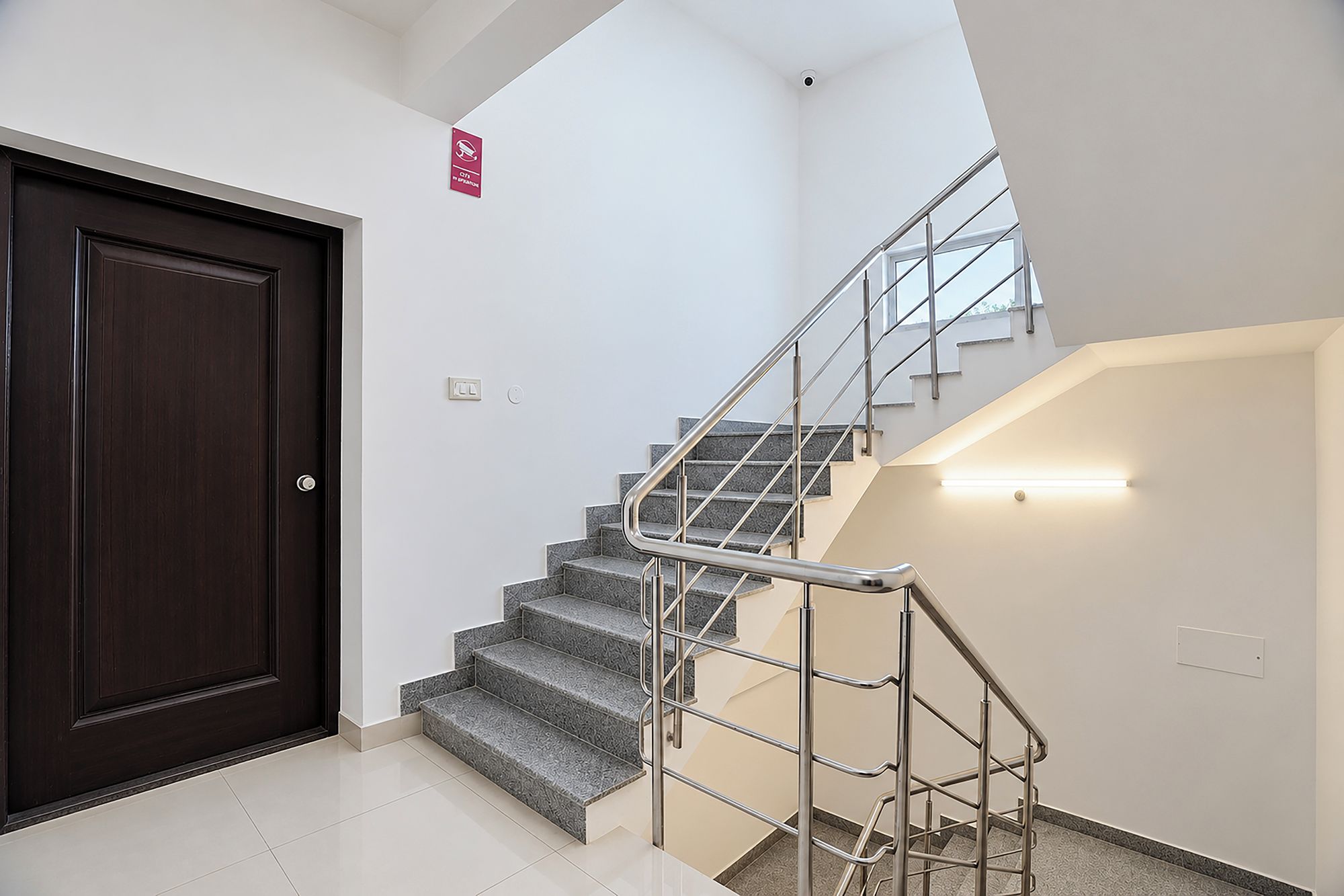 Eine Treppe mit Metallgeländern, einer dunklen Holztür und einer hellen Wand.