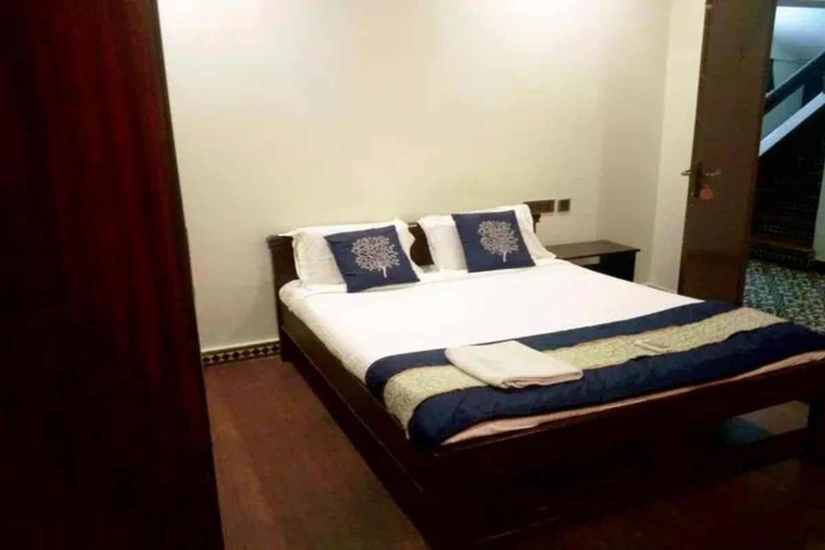 Una cama bien hecha con una colcha blanca y azul, dos almohadas con un diseño de árbol y un cabecero de madera.