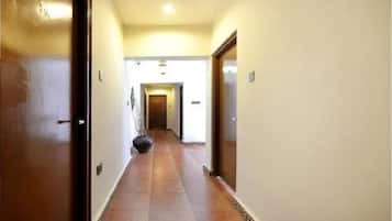 Un couloir avec un sol carrelé, une porte sur la gauche et une porte au fond.