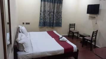 Un lit simple avec une couvre-lit rouge et blanche, une petite table, deux chaises et un téléviseur fixé au mur.