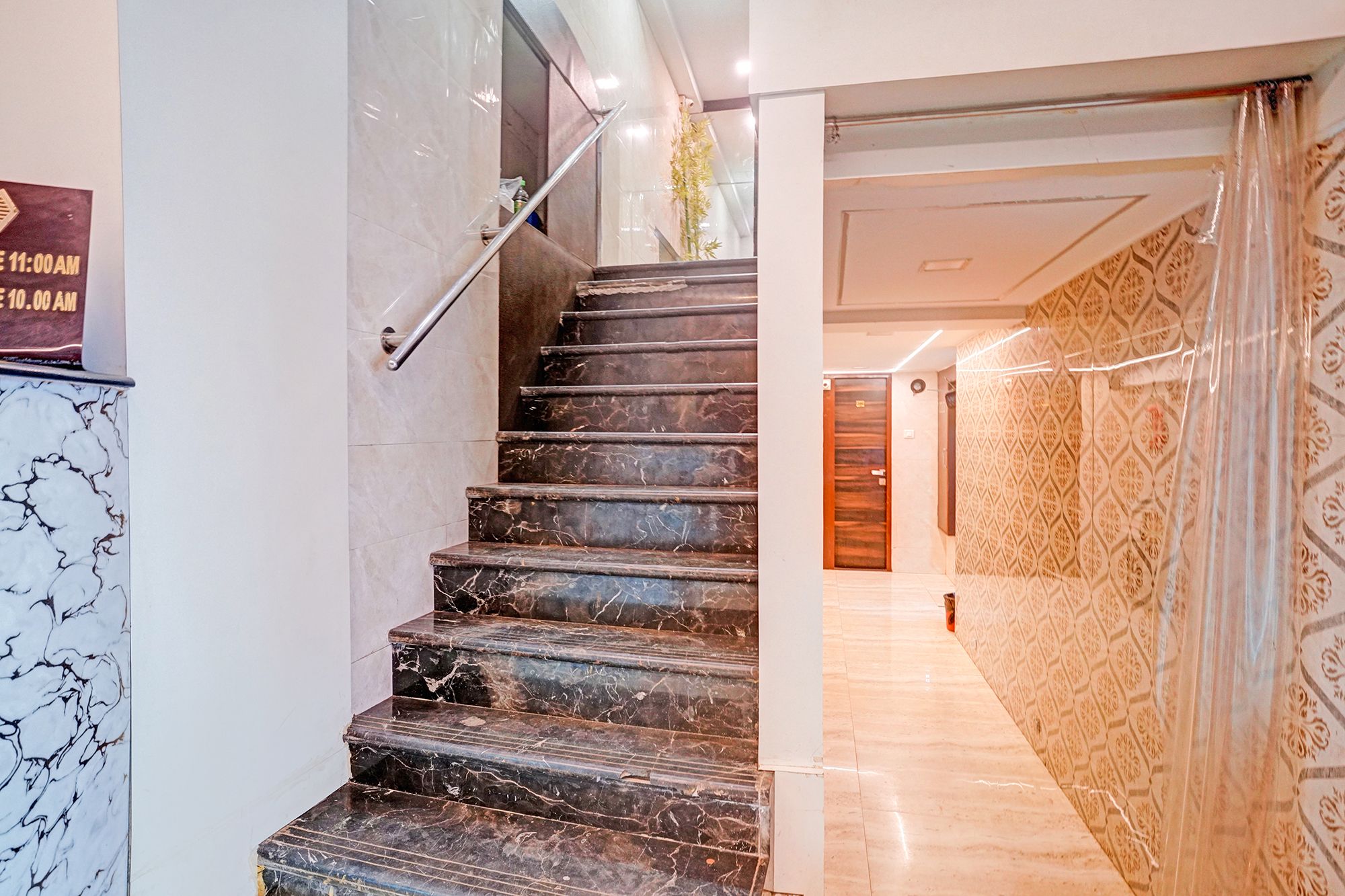 A marble staircase with a handrail leading to a patterned wall and a door.