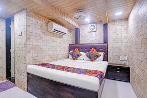 A hotel room with a bed, a nightstand, an air conditioning unit, a ceiling fan, and a wall-mounted light fixture. - FabHotel Qamar (Mumbai)