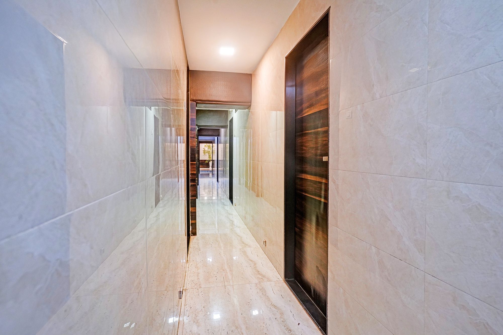 A hallway with a glass partition, a wooden door, and a tiled floor.