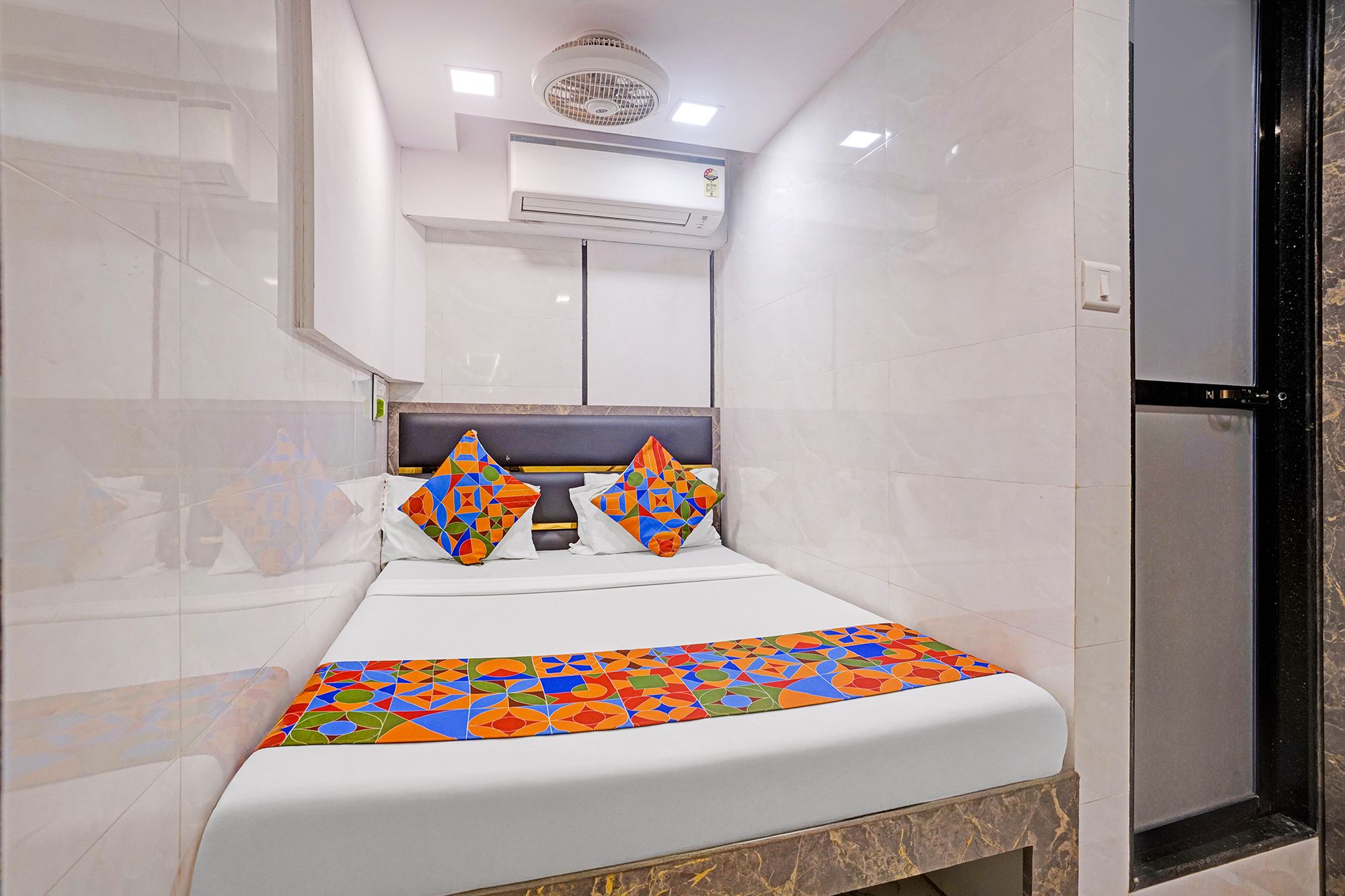A hotel room with a bed, a headboard, an air conditioning unit, and a window.