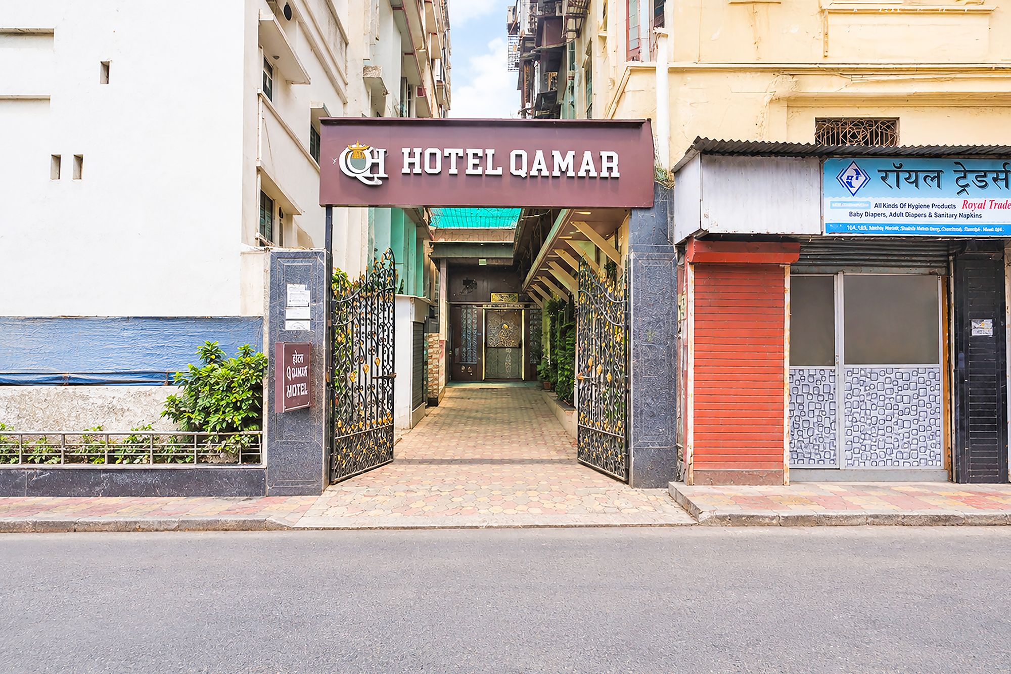 The entrance to Hotel Qamar with a sign above the door, a gated pathway, and a shop with a sign in a foreign language on the right.