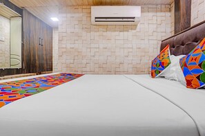 A hotel room with a bed, a colorful rug, a wall-mounted air conditioner, and a wooden door.