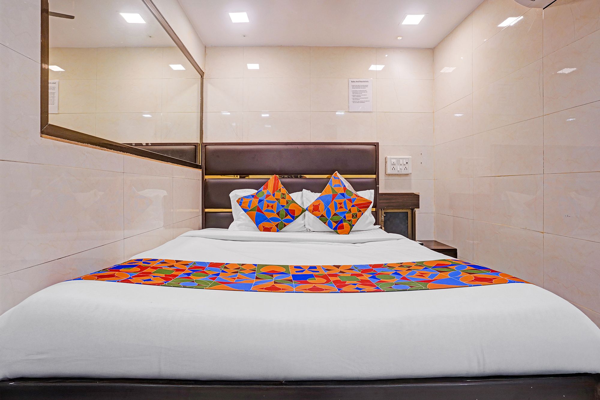 Ett hotellrum med en säng, en sänggavel, en spegel och en skylt på väggen.