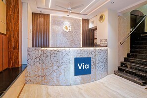 A reception desk with a marble design, a clock, and a staircase.