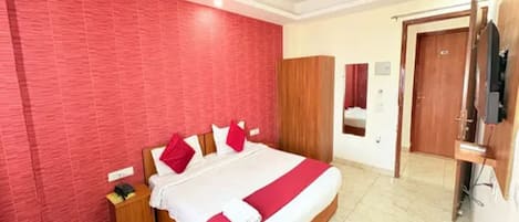 Een hotelkamer met een groot bed, een houten nachtkastje, een rode wand, een plafondventilator en een houten deur.