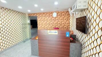 A reception desk with a 'RECEPTION' sign, a clock, and a TV mounted on the wall.