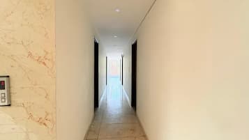 Un pasillo con una pared de mármol a un lado y una pared lisa al otro, que conduce a una habitación luminosa al final.