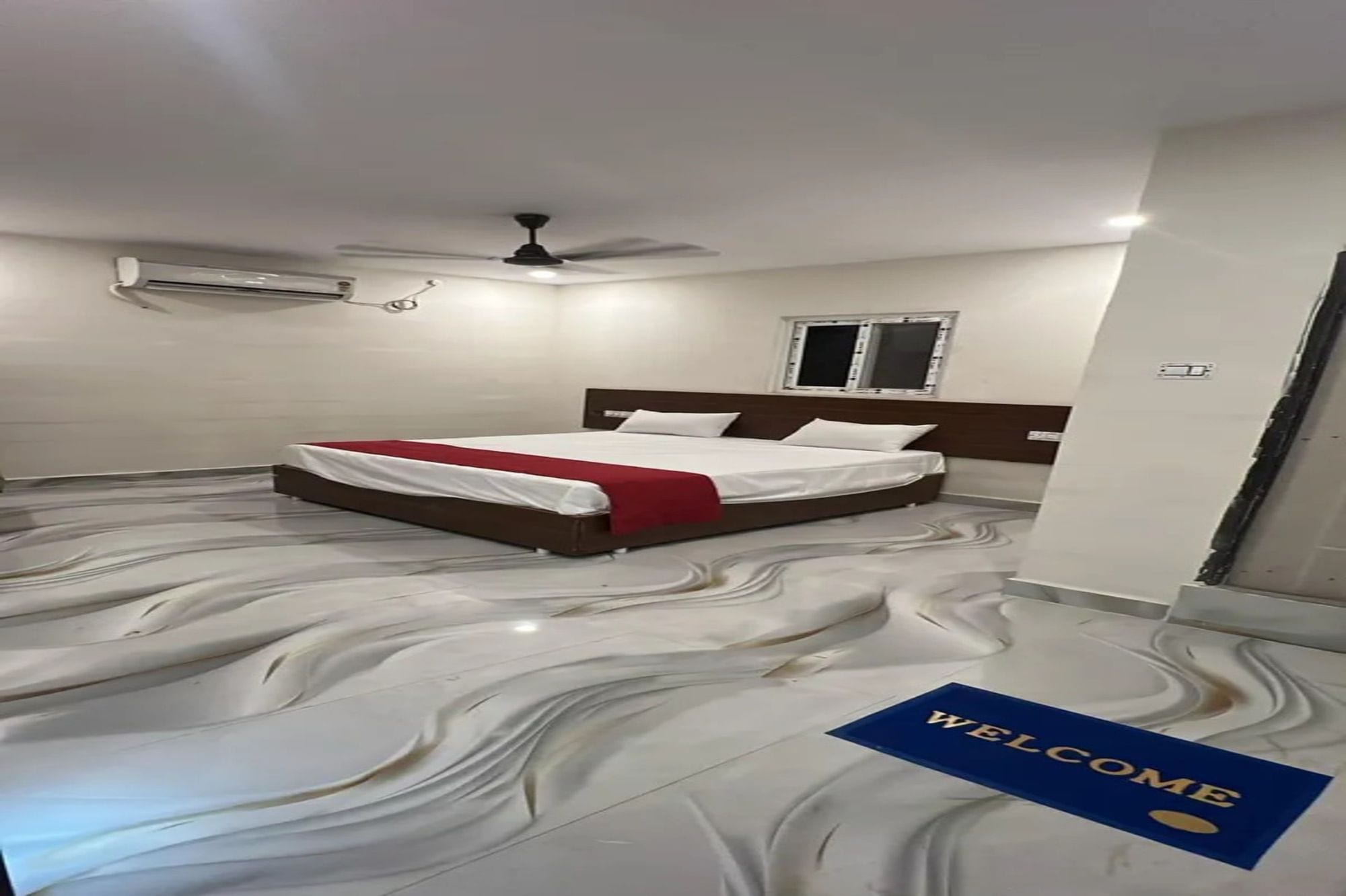 Una camera da letto con un letto, una ventola a soffitto, un condizionatore d'aria, una finestra e un tappetino di benvenuto.