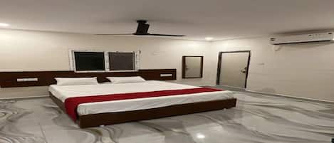 A hotel room with a large bed, a ceiling fan, a window, and an air conditioning unit.