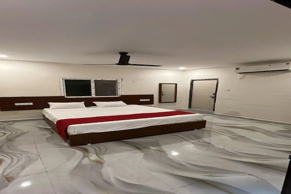 A hotel room with a large bed, a ceiling fan, a window, and an air conditioning unit. - Fabhotel Akhil Dot Inn (Khammam)