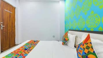 Quarto com cama, almofadas, porta de madeira e um padrão colorido na parede.