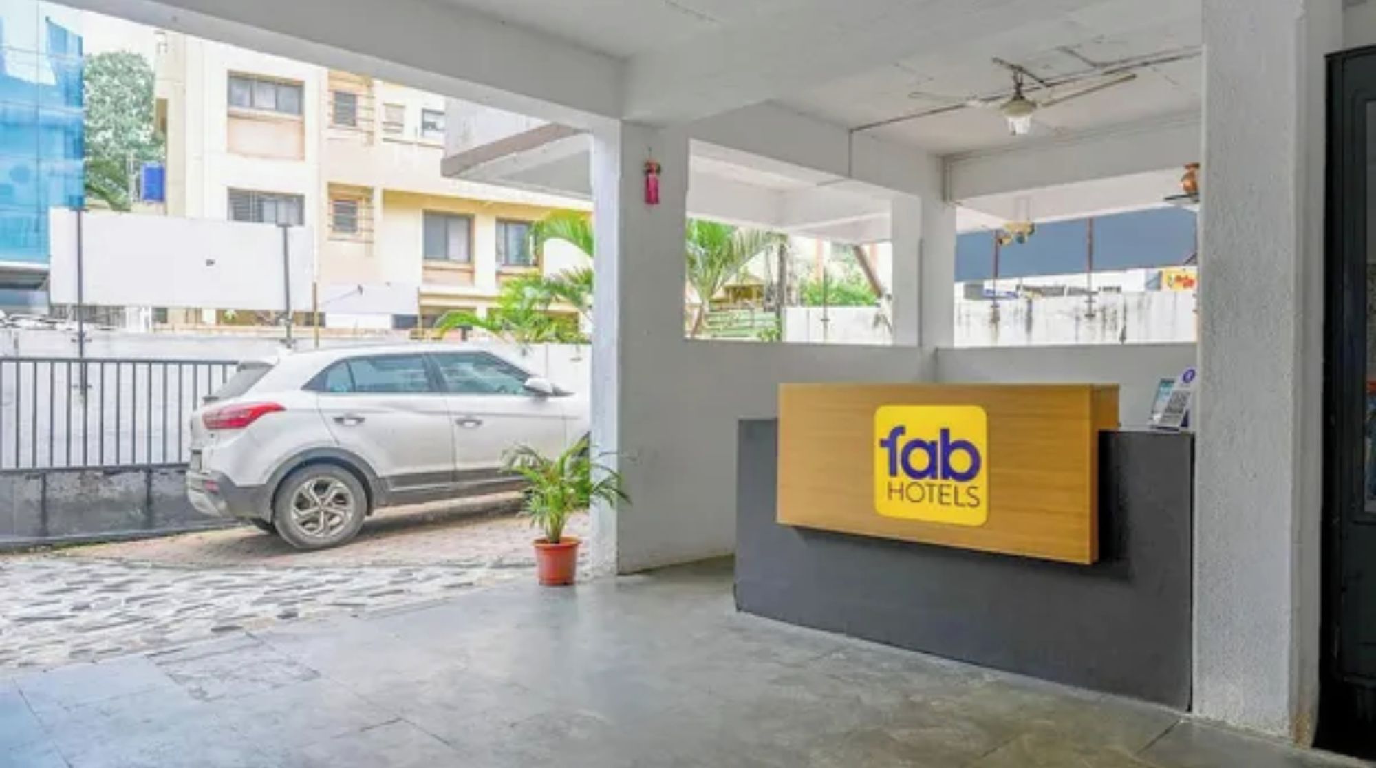 Zona de recepción de hotel con un coche estacionado afuera, un mostrador de recepción y un edificio al fondo.