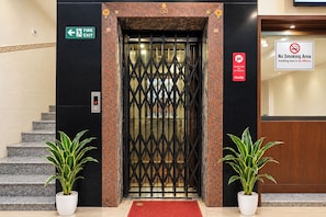 An elevator entrance with a fire exit sign, a no-smoking sign, and a digital elevator display.