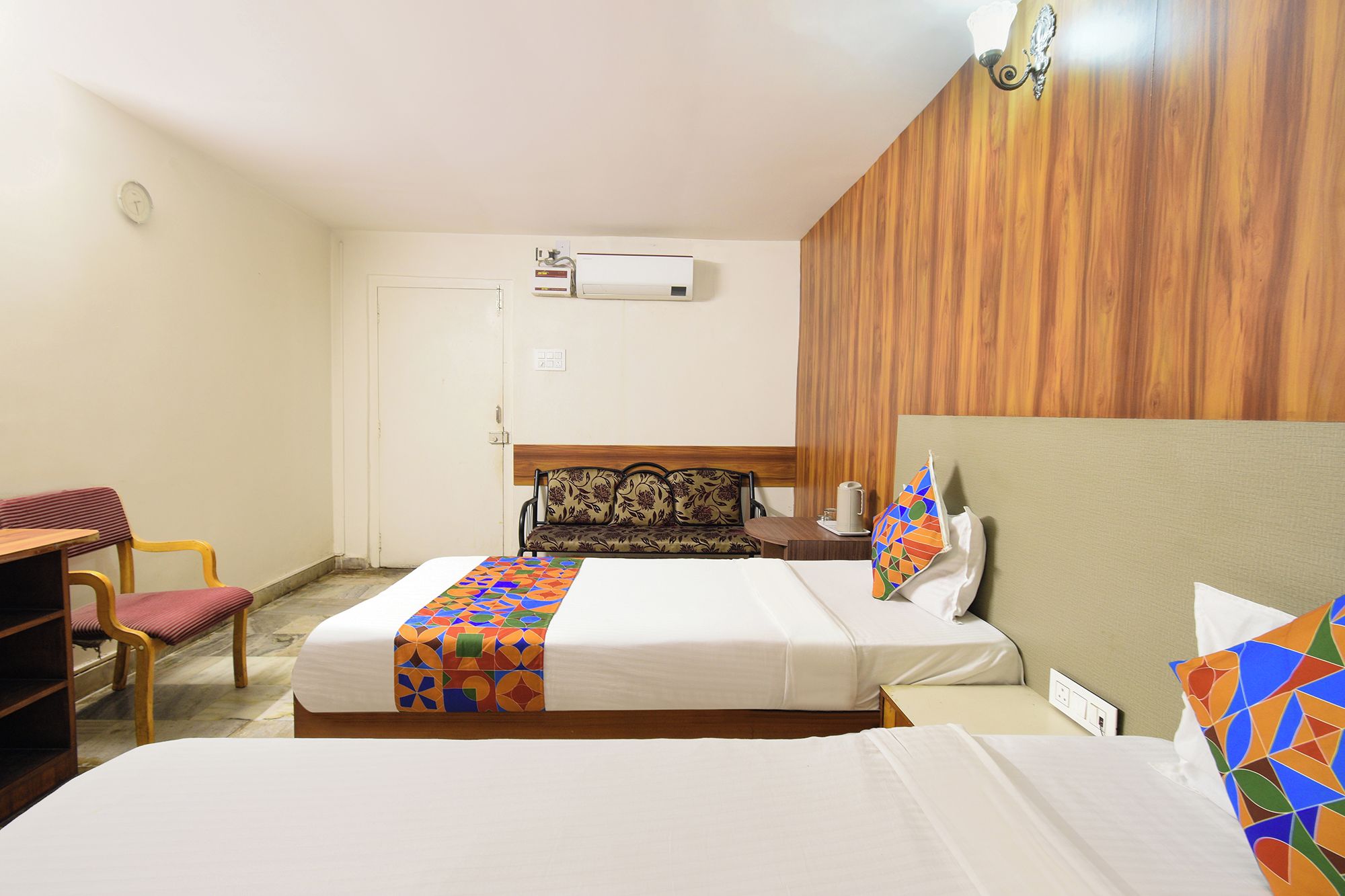 Een hotelkamer met twee bedden, een slaapbank, een bureau en een airconditioning.