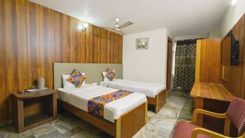 Habitación de hotel con dos camas individuales, cabecera de madera, mesita de noche con lámpara, una silla y un televisor en la pared.
