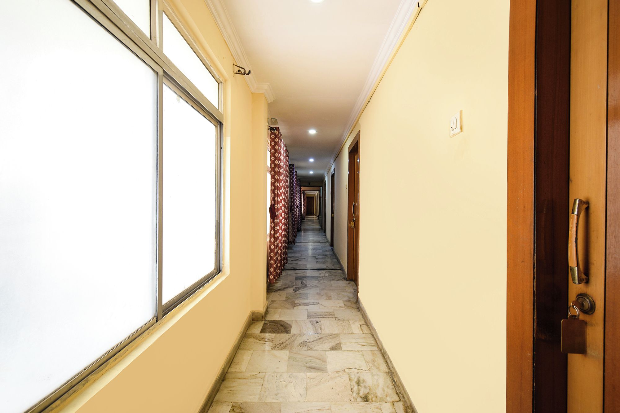 A hallway with a tiled floor, a wooden door on the right, and a window on the left.